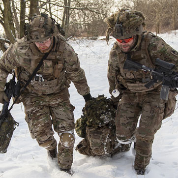 To soldater på øvelse i snevejr. De trækker en såret kollega efter sig.