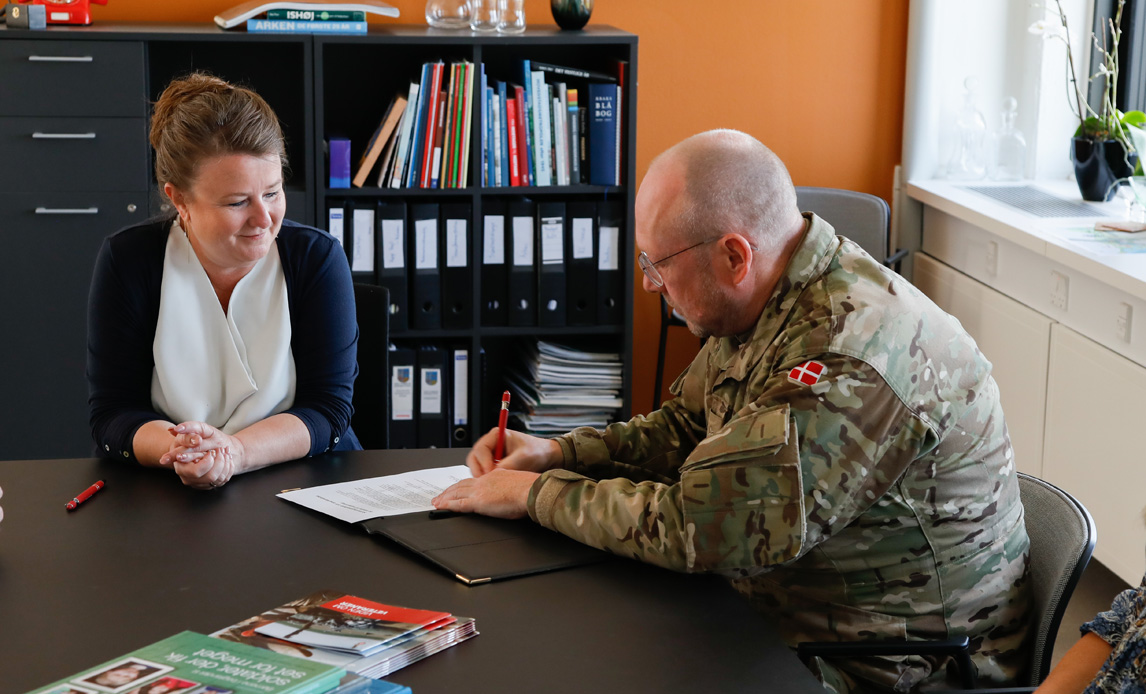 Chef for Veterancentret underskriver dokument, der ligger på et skrivebord.