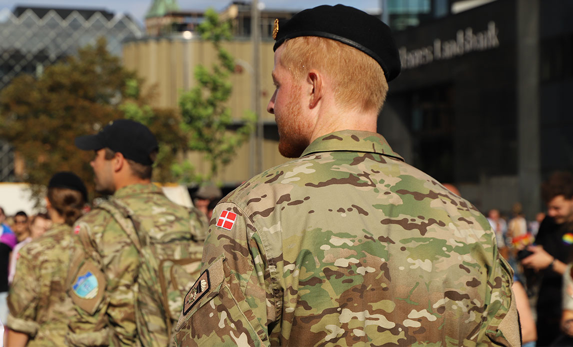 Kortklippet ung mand med baret og uniform går gennem menneskemængde med en uniformeret kollega foran sig. I baggrunden anes Københavns Rådhus.