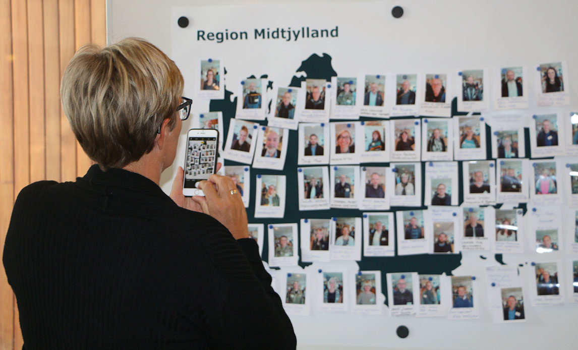 En kvinde tager et foto med sin mobiltelefon af planche af Region Midtjylland, hvor der er sat fotos op af alle aktører i denne region.