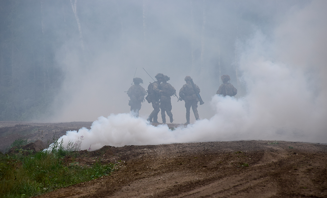 En mark, hvor man gennem et drivende røgslør fra en røggranat kan fornemme fem soldater.