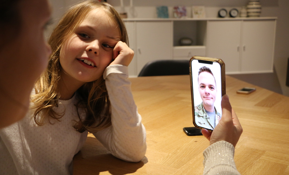 Mor og datter sidder ved spisebord og taler med udsendt soldat via Facetime.