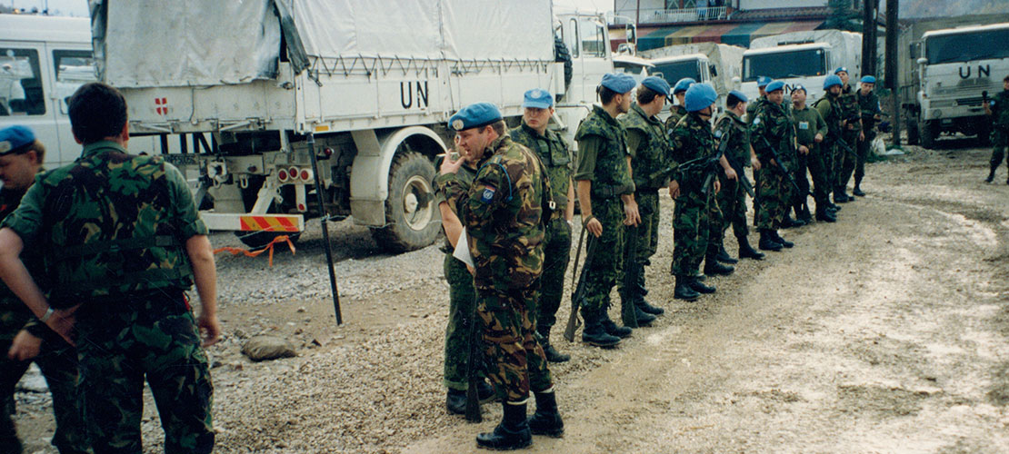 Ældre foto med uniformerede soldater med blå FN-baretter står foran en hvid FN-lastbil og afventer ordrer.