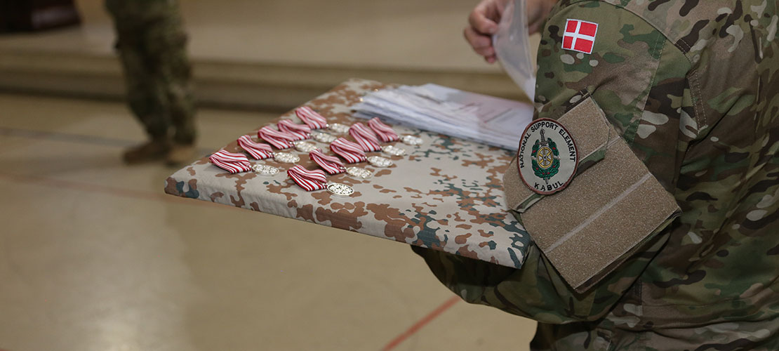 Uniformeret soldat holder bakke med missionsmedaljer, der er skal udleveres.