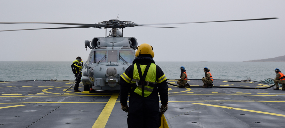 Helikopteren Seahawk står på fregatten Peter Willemoes dæk, der sejler på åbent vand, mens en signalmand står i forgrunden.