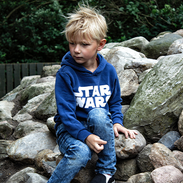 Dreng i alderen 6-8 år sidder på en stenbunke og kigger ned i jorden foran sig.