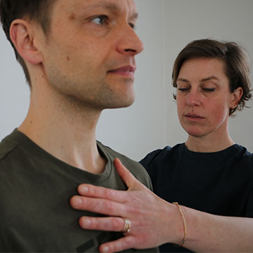 Kvindelig fysioterapeut holder sin hånd på brystkassen af en mand og guider åndedrættet