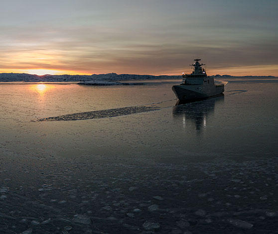 Skibet Ejnar Mikkelsen bryder det let tilfrossede grønlandske ishav i solnedgang.