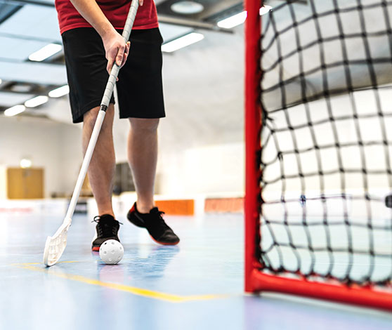 I en hal ses underkroppen på en mand, der holder en hockeystav og spiller floorball.