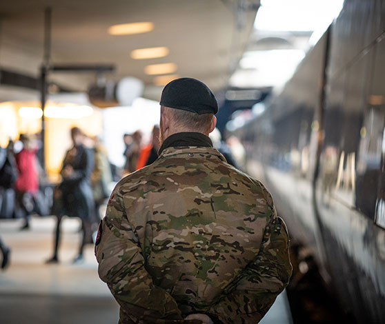 Mand i uniform og med baret står med ryggen til og kigger ud på folk i metroen.