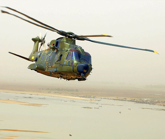 En militær helikopter flyver henover en brunlig flod med tørre og sandede flodbredder.