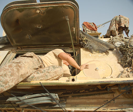 Kvindelig soldat i uniform halvvejs ligger inde i en luge i en sandfarvet panseret mandskabsvogn.