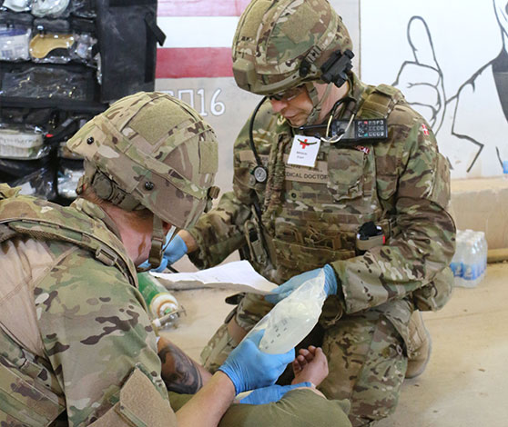 Øvelse i førstehjælp: En soldat ligger på gulvet, mens en læge og en  sanitetsmand behandler med drop.