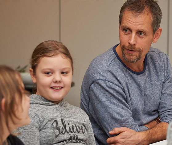 Mand sidder på knæ på gulvet med lukkede øjne, mens kvinde knæler og instruerer ham ved at lægge en hånd på hans brystkasse og ryg.