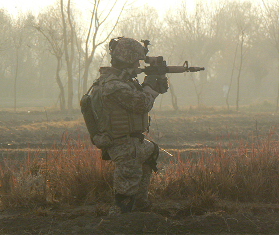En soldat knæler og tager sigte med sit gevær. Der er en tåget dis i baggrunden.